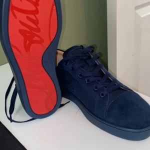 Mörkblå sneakers från Louboutin - Snygga mörkblå sneakers från Louboutin i mocka med klassisk röd sula och ton-i-ton snörning. Skorna har en stilren design med rund tå och diskreta sömmar, perfekta för dig som vill sticka ut med exklusiva detaljer.