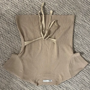 Beige stickad tröja från Zara - Snygg beige stickad tröja från Zara med bred ribbad kant upptill och nertill. Västen har korta ärmar och knytband i nacken för en cool detalj. 