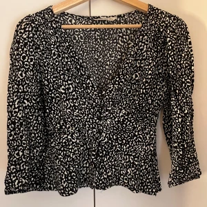 Leopardmönstrad blus från Stradivarius - Svart och vit blus från Stradivarius med leopardmönster. Modellen har v-ringning, knappar framtill och lätt utsvängd midja. Långa ärmar med resår vid ärmslut ger en snygg siluett. Använd ett fåtal gånger.