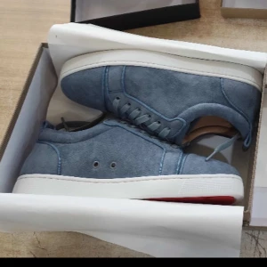 Blå mockasneakers från Christian Louboutin - Snygga blå sneakers i mocka från Christian Louboutin med klassisk vit sula och diskret röd detalj undertill. Skorna har rund tå, snörning och stilren design som passar perfekt till jeans eller chinos. Lyxig känsla med läderfoder och exklusiv finish.