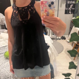 Svart spetsdetaljerad linnetopp H&M - Svart linnetopp från H&M med snygga spetsdetaljer och broderier upptill. Toppen är ärmlös och har en hög halsringning med ett unikt mönster i spetsen som ger en cool och feminin vibe. Perfekt att matcha med jeans eller kjol för en trendig look. Har använts en del.
