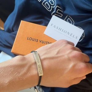 Louis Vuitton LV Space armband - Stilrent armband från Louis Vuitton med svart textilband och en silverfärgad metallplatta med ingraverad logga. Justerbar passform med rund magnetisk låsning. Perfekt accessoar för dig som gillar lyxiga detaljer och minimalistisk design. Äkta såklart köpt på fashionels!🙌🏻