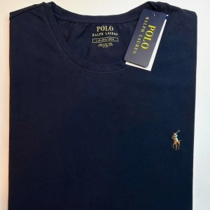 Mörkblå t-shirt från Polo Ralph Lauren - Snygg mörkblå t-shirt från Polo Ralph Lauren med klassisk rund hals och broderad logga på bröstet. Tillverkad i mjuk bomull som känns skön mot huden. Perfekt för en clean och stilren look.