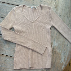 Roséguld glittrig stickad v-ringad tröja - Supersnygg roséguld stickad tröja med v-ringning och diskret glittrig effekt. Tröjan är ribbstickad, har lång ärm och sitter figurnära. Perfekt för dig som gillar en enkel men ändå lite extra look. Passar till både jeans och kjol. Har klippt etiketten, oanvänd, mycket stretch i den.