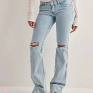 Ljusblå bootcut jeans med slitningar - Säljer ett par ljusblå bootcut jeans med slitna hål på knäna och snygg broderad detalj i rosa på backfickorna