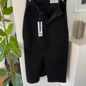 Svart lång Jeanskjol!  - Snygg svart lång jeanskjol från Noisy May med en klassisk design. Kjolen har en slits framtill och stängs med dragkedja och knapp. Perfekt för en stilren look.prislappar kvar! Den är helsvart inga skuggor osv som på bilden.