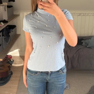 T-shirt med pärlor  - Supersöt ljusblå ribbad topp från Lindex med korta ärmar och hög hals. Toppen är dekorerad med små pärlor framtill💕 Säljer den pga av att den inte kommer till användning längre. Är 146/152 i barnstorlek men skulle säga att det passar xs/s också🥰