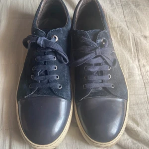 Mörkblå sneakers från Lanvin mocka - Snygga mörkblå sneakers från Lanvin i mocka med rund tå och snörning. Skorna har en kontrasterande mörkblå tå i skinn och vit sula. Baksidan har en detalj i vinrött. Perfekta för dig som gillar stilrena och lyxiga sneakers.