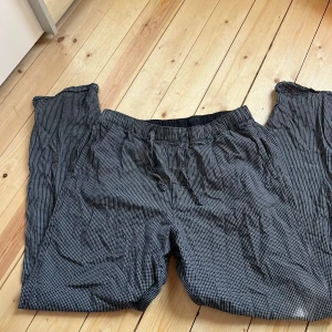 Svarta rutiga byxor från H&M, S - Svarta byxor från H&M i storlek S med vitt rutmönster. Byxorna har resår i midjan och snörning för extra komfort. Tillverkade i mjukt bomullsmaterial, raka ben och avslappnad passform. Perfekta för en chill och stilren look.