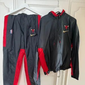 Chicago Bulls Nike träningsset - Snyggt träningsset från Nike och Chicago Bulls med jacka och byxor i svart och rött. Perfekt för basketfans!