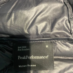 Svart dunjacka Peak Performance M - Säljer en svart dunjacka från Peak Performance i storlek M. Jackan har huva, dragkedja framtill och två fickor med dragkedja. Lätt och smidig modell med diskret logga på bröstet. Perfekt för kyliga dagar och enkel att matcha. Den har två jätte små hål som inte syns eller är störigt. Arnas är den inte använd så jätte mycket då jag haft den några år men knappt använd alls. Jag köpte den för dyrt pris och då den inte använd mycket alls heller. Kom med bud arnas.