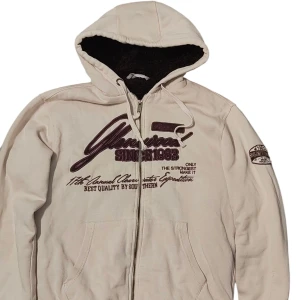 Beige hoodie från Southern med tryck - Beige hoodie från Southern med mörkbrunt teddyfoder i huvan och coolt tryck framtill. Dragkedja hela vägen, snörning i huvan och två fickor. Perfekt för dig som gillar streetwear och vill ha något både snyggt och bekvämt.