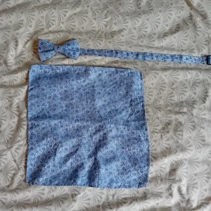 Blå blommig fluga & näsduk Notch - Snyggt set med fluga och matchande näsduk från Notch. Båda i ljusblått tyg med små blommor i olika blå nyanser. Perfekt för att lyfta din outfit med en färgklick och stilren detalj. Flugan har justerbart band och näsduken är fyrkantig. Använd få gånger. 