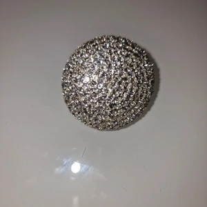 Glittrig silverfärgad ring - Stor, rund cocktailring i silverfärg med massor av gnistrande stenar över hela ovansidan. Ringen har en bred, elastisk ringdel som gör att den passar de flesta. Perfekt för dig som vill sticka ut med ett riktigt statement-smycke.