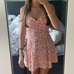 Blommig kort sommarklänning  - Supersöt kort klänning med blommigt mönster från Gina tricot. Klänningen har smala axelband, knyt i ryggen och öppen rygg. 