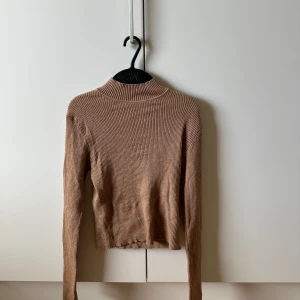 Beige ribbad polotröja Pull&Bear - Säljer en beige ribbad polotröja från Pull&Bear. Tröjan har lång ärm, tight passform och hög krage. Perfekt att styla med jeans eller kjol för en clean look. Materialet är mjukt och stretchigt, vilket gör den riktigt skön att bära.