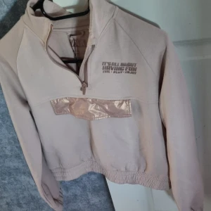 Beige half zip tröja från Zara - Beige långärmad tröja från Zara med half zip och trycket 'It's all about having fun' på bröstet. Tröjan har en glansig detalj på magen och elastisk nederkant. Perfekt för en chill och avslappnad stil.