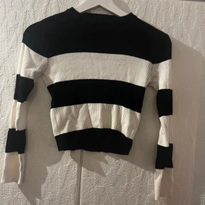 Randig svartvit ribbad tröja - Snygg ribbad tröja med breda svarta och vita ränder. Modellen är croppad och har lång ärm. Perfekt för dig som gillar en stilren men ändå trendig look. Materialet är stretchigt och sitter skönt på kroppen.