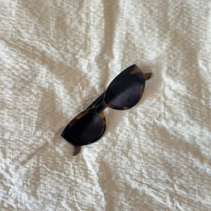Bruna cat eye-solglasögon från Lindex - Snygga cat eye-solglasögon från Lindex i brunmelerad plast. Glasögonen har markerad båge och är tillverkade av återvunnen plast. Perfekt accessoar för att lyfta din look med en retrovibe.