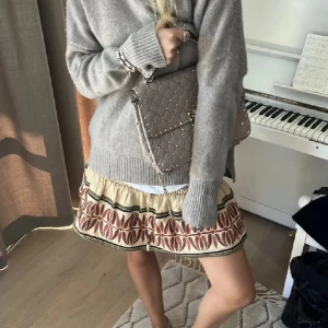 Zara Minikjol - Supersöt minikjol från Zara i beige bomull med elastisk midja och snörning med pärlor. Kjolen har ett unikt rödbrunt och grönt mönster längs kanten och smockad överdel. Perfekt för dig som gillar boho-vibes och vill sticka ut lite extra. Stockholmstil. I 100% bomull och i nyskick. 