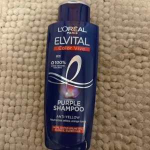 L'Oréal Elvital Color Vive Purple Shampoo - Lila schampo från L'Oréal Elvital Color Vive, 200 ml, speciellt för att neutralisera gula och orange toner i blont, slingat eller silverfärgat hår. Kommer i en mörklila plastflaska med röd och vit text. Perfekt för dig som vill fräscha upp hårfärgen.