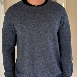 Oscar Jacobson tröja - Säljer en stilren mörkblå stickad tröja från Oscar Jacobson i storlek M. Tröjan har rund halsringning, ribbade muddar och är långärmad. Perfekt för lager-på-lager och funkar året runt. Enkel att matcha med både jeans och chinos.