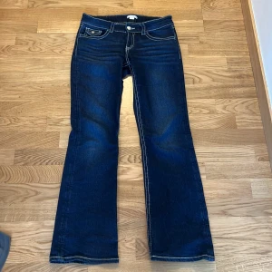 Mörkblå bootcut jeans Gina Tricot - Snygga mörkblå jeans från Gina Tricot i bootcut-modell med kontrasterande vita sömmar. Klassisk femficksdesign med lock på bakfickorna och knappdetaljer. Jeansen har låg midja och är tillverkade i stretchig denim för skön passform.