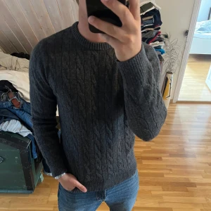 Mörkgrå kabelstickad - Kabelstickad tröja från Dressmann. Bara använd några gånger men krympte i tvätten så passar inte riktigt längre. Storlek L men sitter som en M nu.