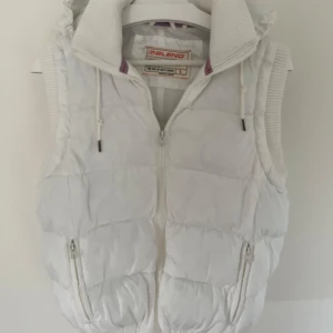 Vit dunväst från Blend - Säljer en snygg vit dunväst från Blend med dragkedja och huva. Västen har ribbade detaljer och dragsko vid huvan för justerbar passform. Perfekt till våren/sommaren! Säljer pga den är för liten men den är i mycket bra skick. 