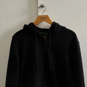Svart hoodie från Boss - Tjena, säljer en snygg svart zip hoodie från Boss med dragkedja och justerbar huva. Skicket är väldigt bra, köpte den för ett par månader sen men ser sprillans ny ut. Priset går att diskutera i DM:)