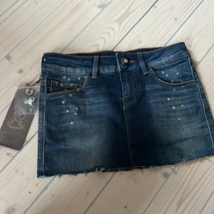 Blå jeanskjol från Bershka - Snygg blå jeanskjol från Bershka med slitna detaljer och rå kant. Kjolen har klassisk femficksdesign och knappgylf. Perfekt för en avslappnad stil.