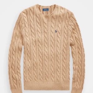 Beige stickad tröja från Polo Ralph Lauren - Säljer en snygg beige stickad tröja från Polo Ralph Lauren med kabelstickat mönster och den klassiska loggan på bröstet. Tröjan har långa ärmar och rund halsringning. OBS: tröjans märke är vitt, och lite annolrunda beige som man ser på bild 2. Skriv för fler bilder🙏🏻