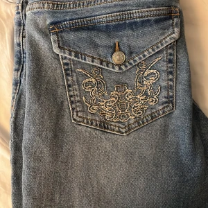 Blå jeans med broderad ficka - Snygga blå jeans med en unik broderad design på bakfickan. De har en klassisk femficksmodell och dragkedja framtill. Perfekta för en avslappnad stil. Low waist
