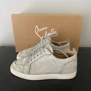  Christian Louboutin skor - Snygga grå sneakers i mocka från Christian Louboutin med den ikoniska röda sulan. Skorna har snörning och en stilren design som passar perfekt för en trendig look. Levereras med originalkartong.