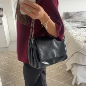 Svart axelväska med kedja - Snygg svart axelväska i skinn från Zara. Väskan har en kedja som axelrem vilket ger en cool touch. Perfekt för att bära dina nödvändigheter med stil. Aldrig använd💗