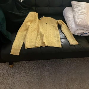 Gul stickad tröja från Ralph Lauren - Säljer en snygg gul stickad tröja från Ralph Lauren. Tröjan har ett klassiskt flätmönster och långa ärmar. Perfekt för att hålla sig varm och stilren under kyligare dagar.  Passar bra till både jeans och kjol. Pris kan sänkas vid snabb affär