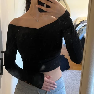 Svart offshoulder topp från NA-KD - Säljer en snygg svart offshoulder topp från NA-KD. Toppen är croppad och har långa ärmar med en ribbad struktur. Perfekt för en stilren look.