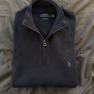 Mörkblå halvzip från Ralph Lauren - Säljer en stilren mörkblå tröja från Ralph Lauren i Pima bomull. Tröjan har en halv dragkedja och en liten broderad logotyp på bröstet. Perfekt för en avslappnad men snygg look. Nypris 2400kr