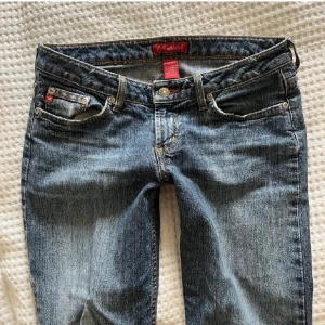 Blå jeansbyxor med bootcut - Köpta för 1500kr. Midjemått: 39 och innerbneslängd: 80 cm. Snygga blå jeansbyxor med en klassisk bootcut-stil. Byxorna har en låg midja och är tillverkade i jeansmaterial. De har en dragkedja och knappar framtill samt dekorativa sömmar och fickor med detaljer.