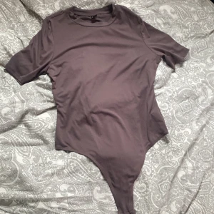 Brun bodysuit från Shein - Säljer en stilren brun bodysuit från Shein. Den har korta ärmar och en rund halsringning. Perfekt för att matcha med jeans eller kjol för en enkel och snygg look.