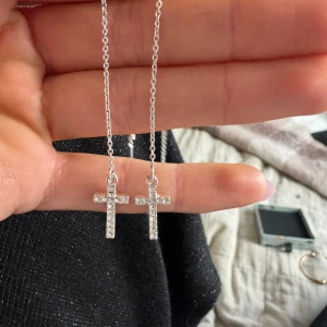 Silverfärgade korsörhängen - Snygga silverfärgade örhängen med hängande kors med glittriga stenar. Endast använda en gång. Köpta på glitter💕💕