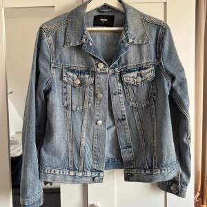 Jeansjacka  - Snygg blå jeansjacka från Bik Bok med klassisk design. Jackan har långa ärmar och knappar framtill samt på bröstfickorna. Perfekt för en avslappnad stil.