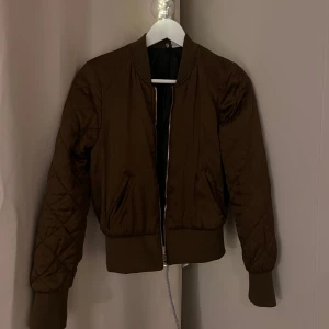 Brun bomberjacka - Snygg brun bomberjacka med dragkedja och quiltade detaljer från H&M. Jackan har långa ärmar och ribbade muddar vid ärmslut och nederkant. Har en liten fläck vid fickan (har inte testat att få bort det) 