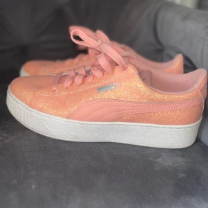 Glittriga sneakers från Puma - Snygga glittriga sneakers från Puma i en härlig persikofärg. Skorna har en vit sula och matchande snörning. Perfekta för att ge din outfit en extra touch av glamour. Använda max 1 gång! Som nya! Ny pris 600kr