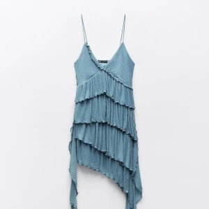 Blå asymmetrisk klänning med volanger - Snygg blå klänning med smala axelband och asymmetrisk design. Klänningen har flera lager av volanger som ger en unik look. Perfekt för en somrig dag eller en speciell kväll. 