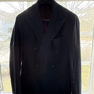 Svart kavaj från Elson - Elegant svart kavaj från Elson med dubbelknäppning och klassiska slag. Perfekt för formella tillfällen. Kavajen har en stilren design med diskreta fickor och knappar framtill.