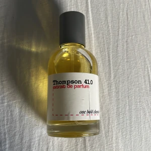 Thompson 41.0 Extrait de Parfum - Elegant och djärv parfym i en rund glasflaska med svart kork. Etiketten är vit med röd och svart text. Perfekt för den som söker en unik doftupplevelse.
