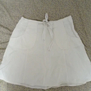 Vit kjol från L.O.G.G. - Säljer en vit kjol från L.O.G.G. med knappar och fickor. Kjolen har en knytning i midjan och är perfekt för sommardagar. Tillverkad i ett lätt och bekvämt material. Midjan ca 80cm, längd ca 48cm. Skriv gärna om du vill ha mer information om kjolen. 