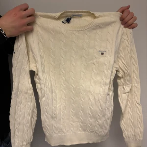 Vit stickad tröja från Gant - Säljer en stilren vit stickad tröja från Gant med klassiskt flätmönster. Tröjan har långa ärmar och rund halsringning. 