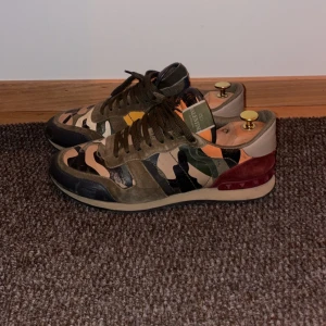 Camouflage sneakers från Valentino - Snygga sneakers från Valentino med ett coolt camouflage-mönster i gröna och beige toner. Skorna har snörning och detaljer i mocka och skinn, vilket ger en lyxig känsla. Perfekta för dig som vill sticka ut med stil.